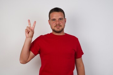 Fototapeta premium Young caucasian man wearing red t-shirt over white background showing and pointing up with fingers number two while smiling confident and happy.