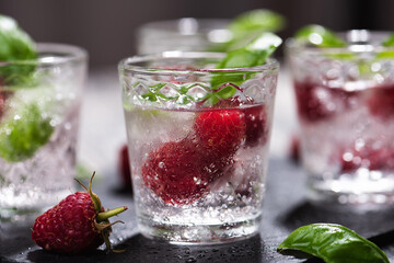 Fototapeta na wymiar Alcohol shots of berries cocktail with a raspberry and basil on black stone tray. Glass of sparkling water on wooden table