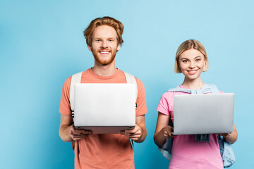 redhead and blonde students holding laptops on blue