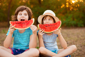 Funny happy children eating watermelon in park at sunset