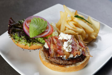 Juicy beef burger with cheese, bacon, tomato, lettuce, dressings, avocado, red onion and accompanied by french fries.
