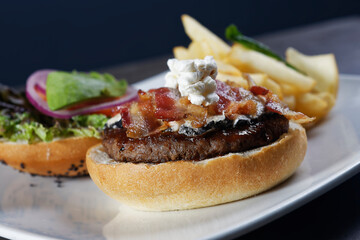 Juicy beef burger with cheese, bacon, tomato, lettuce, dressings, avocado, red onion and accompanied by french fries.