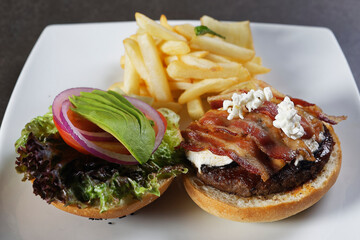 Juicy beef burger with cheese, bacon, tomato, lettuce, dressings, avocado, red onion and accompanied by french fries.