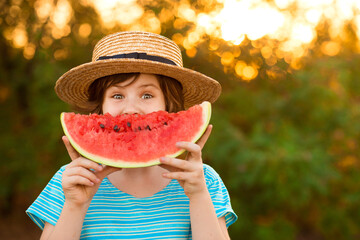 Funny happy child girl in hat girl hides her face behind slice of watermelon outdoors in park