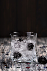 Sparkling alcoholic cocktail with a blackberry on wooden table with glitter stars. Detox water