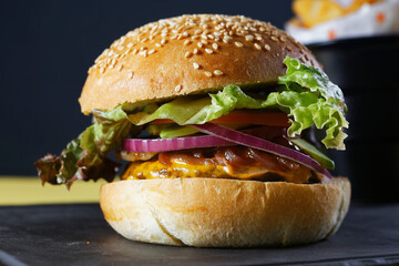 Juicy beef burger with cheese, bacon, tomato, lettuce, dressings, avocado, red onion and accompanied by french fries.