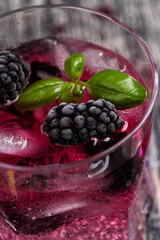 Sparkling alcoholic cocktail with a blackberry and basil on wooden table with glitter stars. Detox water