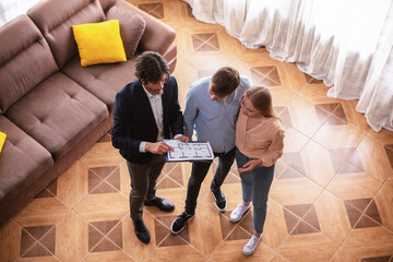 Realtor showing house plan to couple of young clients indoors, above view