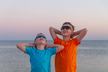 Two boys stand by the sea in sunglasses. Bright t-shirts on children. The guys like to relax on the ocean.