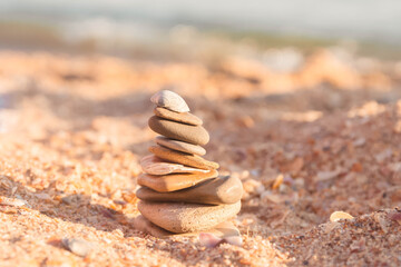Fototapeta na wymiar Tower of flat stones on the beach by the sea. Beautiful stones on the sand in the form of a pyramid. White shell on top of the pyramid.
