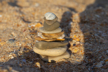A tower of flat stones with a white shell on the beach by the sea. Hello sea. Stone pyramid on the sand.