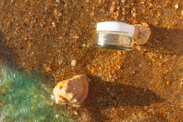 Mineral sea cosmetics for beauty. Can of cream on the sea. Sea water in a cream or transparent gel. Shells on the Golden sand by the ocean.