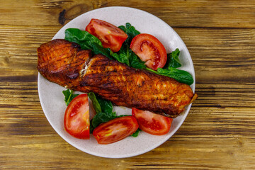 Grilled salmon fillet with spinach and tomatoes on wooden table. Top view