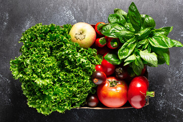 Fresh farmers food delivery concept. Organic vegetables, fruit and greens in the box on black background top view.