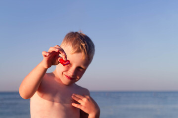 Hello, sea! Sea background. A boy on the beach by the sea with a red heart in his hand. The child...