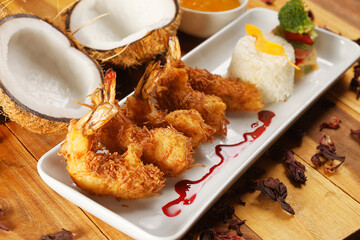 Breaded shrimp with Coconut shell in Jamaican sauce, accompanied by steamed rice and garnished with pumpkin and carrot vegetables.