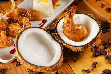 Breaded shrimp with Coconut shell in Jamaican sauce, accompanied by steamed rice and garnished with pumpkin and carrot vegetables.