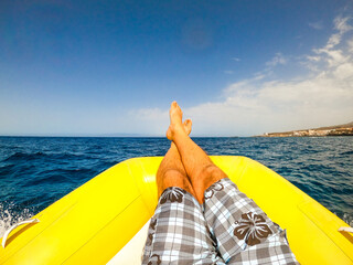 close up and portrait of legs of man lay down on a boat or dinghy in the middle of the sea looking...