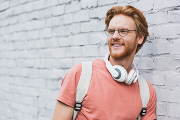 redhead student in glasses and wireless headphones looking away