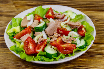 Tasty tuna salad with lettuce and fresh vegetables on wooden table