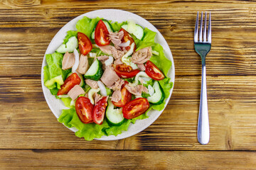 Tasty tuna salad with lettuce and fresh vegetables on wooden table. Top view