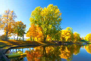 Beautiful autumn city park. Sunny landscape. Small lake in park arrounded trees. Yellow catamaran.