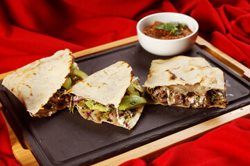 Traditional Oaxacan tlayuda stuffed with meat, melted cheese and avocado, accompanied by red chili sauce.