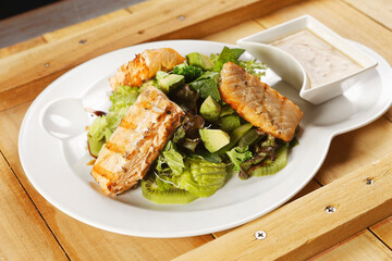 Tilapia fish fillet salad with lettuce, cabbage, kiwi, broccoli, and avocado.