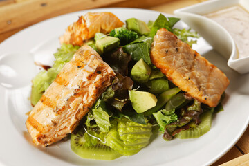 Tilapia fish fillet salad with lettuce, cabbage, kiwi, broccoli, and avocado.