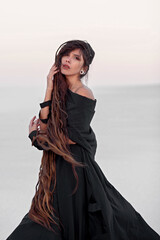 Naklejka premium Girl with dreadlocks in a dress in the desert on white sand. Sunset