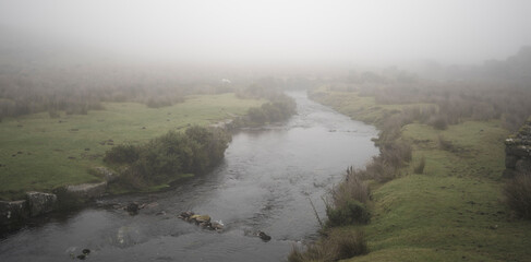Rive flowing through fields on a foggy day