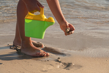 Little kid playing with bucket toys and walking on the beach at sunset.