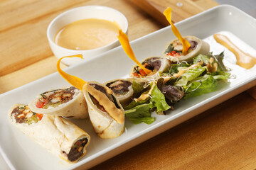 Chicken wrap with beans and peppers accompanied by salad and cheddar cheese dressing.