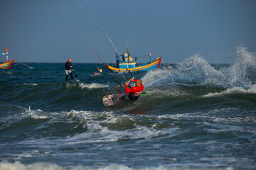 Obraz premium Kitesurfing on the waves of the sea in Mui Ne beach, Phan Thiet, Binh Thuan, Vietnam. Kitesurfing, Kiteboarding action photos. Kitesurf In Action against vietnamese boats