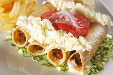 Golden chicken tacos with lettuce, fresh cheese and tomato accompanied by french fries.
