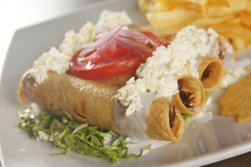Golden chicken tacos with lettuce, fresh cheese and tomato accompanied by french fries.