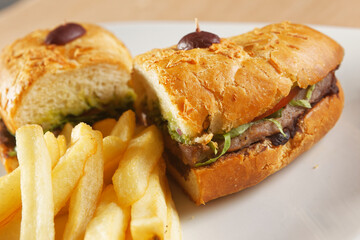 Beef baguette with tomato, lettuce, avocado and dressings accompanied by french fries.
