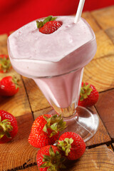 Strawberry shake on wooden table with fresh strawberries around.