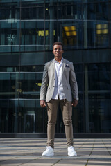 A young attractive black man in a business suit stands in full growth against the background of the city.
