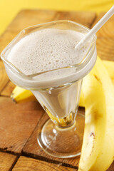 Banana milkshake on wooden table with fresh bananas around.