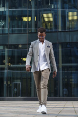 Young attractive black man in a business suit smiles and walks against the backdrop of an office building.