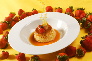 Vanilla custard with caramel and strawberry on yellow tablecloth.