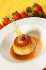 Vanilla custard with caramel and strawberry on yellow tablecloth.