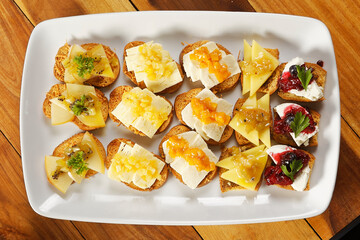 Snacks of toasted bread with Mozarella cheese, fresh cheese and Manchego cheese with strawberry, kiwi and pineapple marmalade.