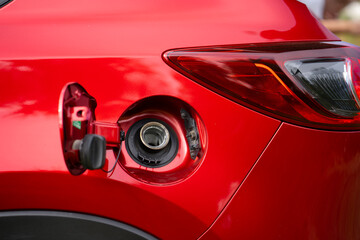 An open fuel tank cap of a red car for filling gasoline or diesel fuel into the gas tank. The back...