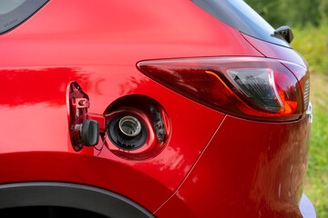 An open fuel tank cap of a red car for filling gasoline or diesel fuel into the gas tank. The back...