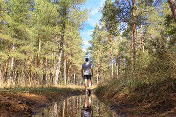 Obraz premium Reflection of an unrecognizable sportsman man in the puddle of a forest road