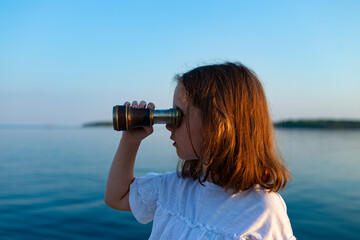 Funny little girl looking through vintage binoculars on sunny summer day. Rovinj town in background. Travel and adventure concept.
