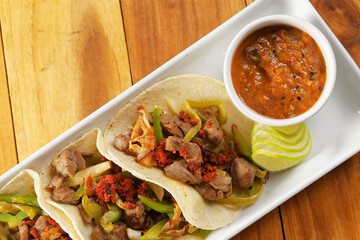 Angus beef tacos with chorizo, pepper and onion accompanied by tomato and chili sauce.