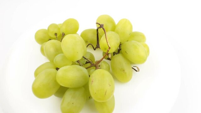 Ripe juicy grapes rotate on a plate. Close-up of a bunch of white grapes. Fresh bunch of juicy grapes rotate on a white background.